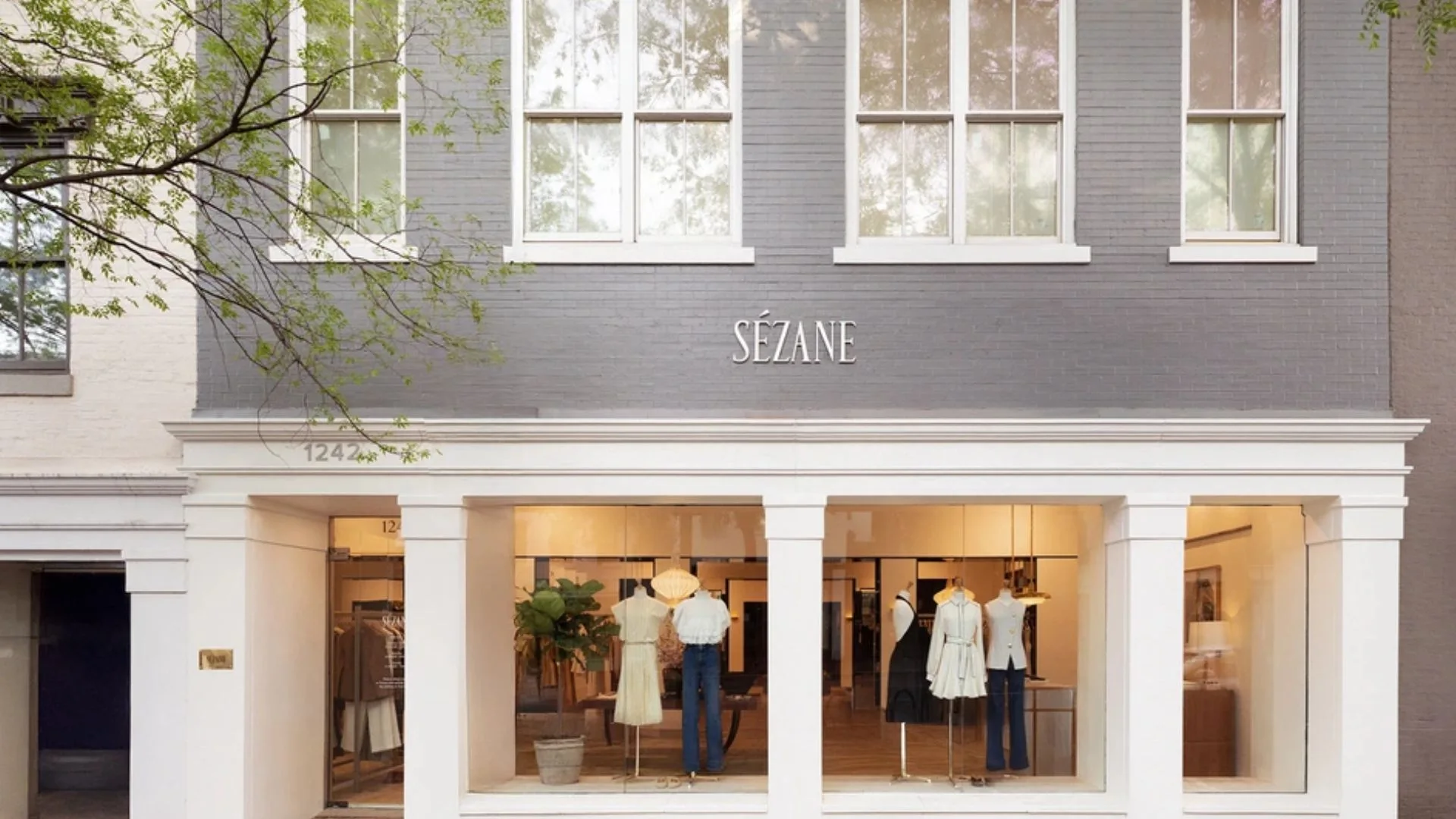Sezane clothing boutique storefront with gray brick walls, large display windows, mannequins, and the address 1242½ above the entrance.