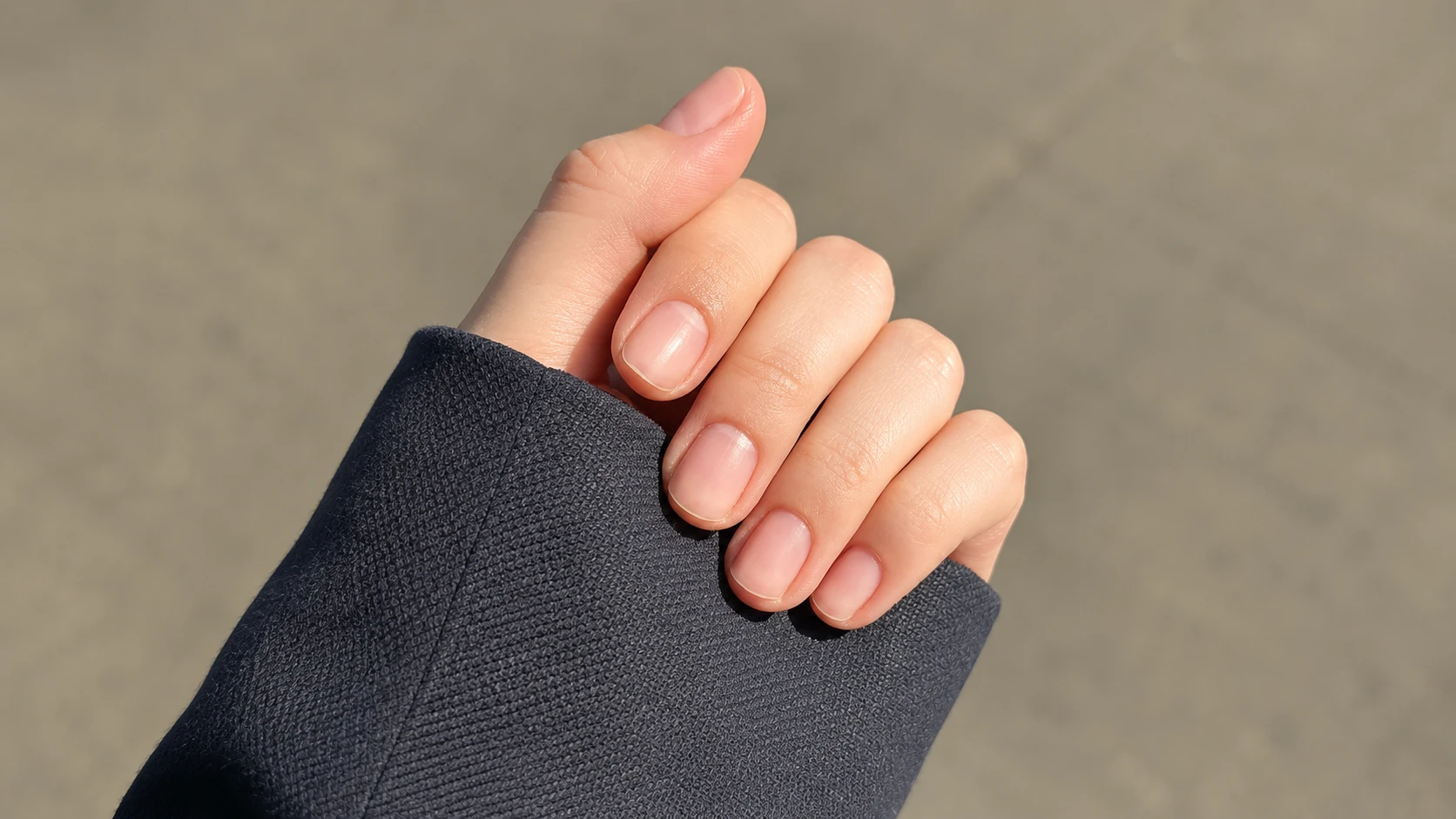 Short natural nails on a gently curled hand framed by a dark sleeve in warm outdoor sunlight