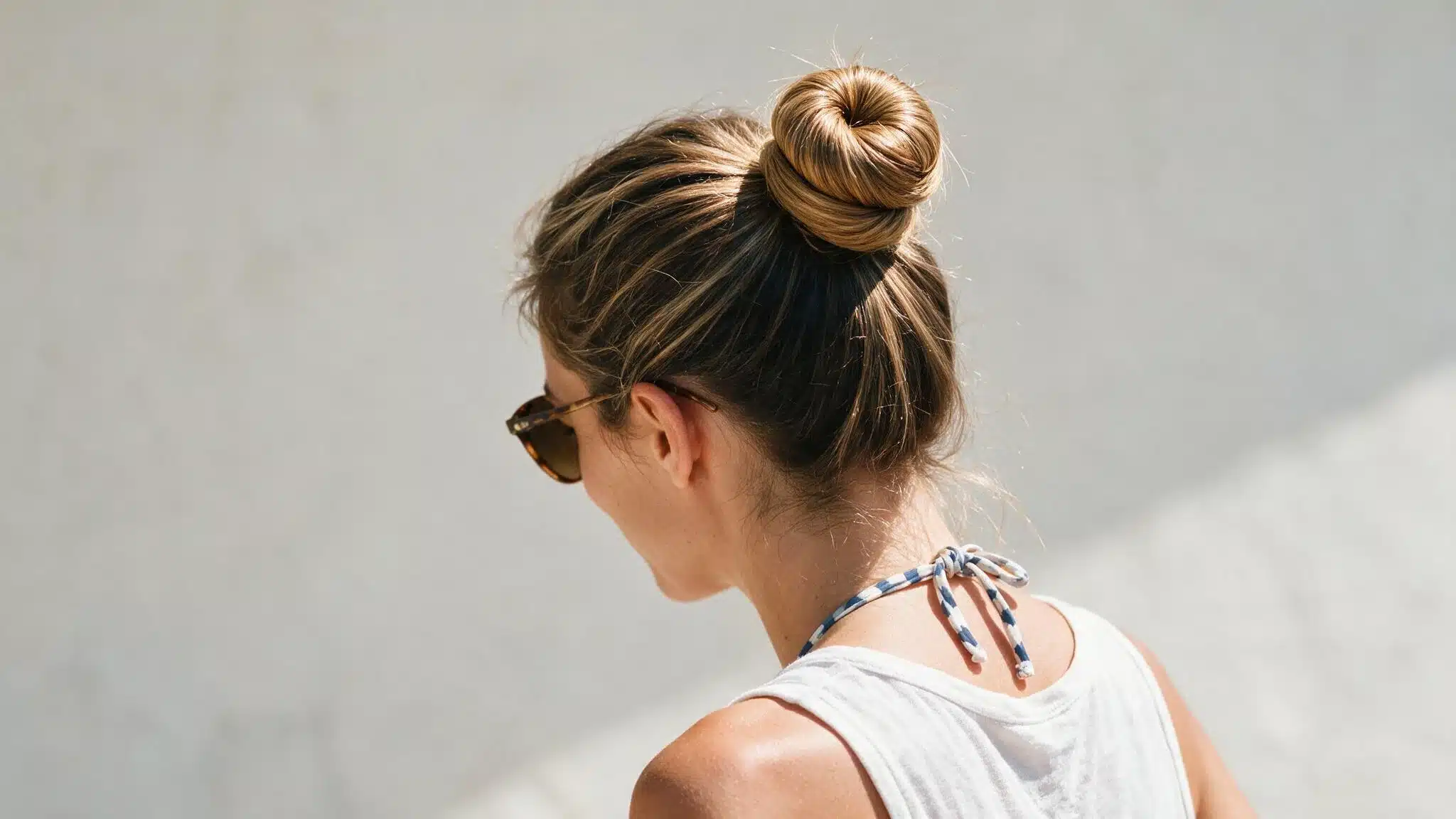 woman with long hair wearing a simple top knot slightly behind the crown, with a compact bun and natural flyaways