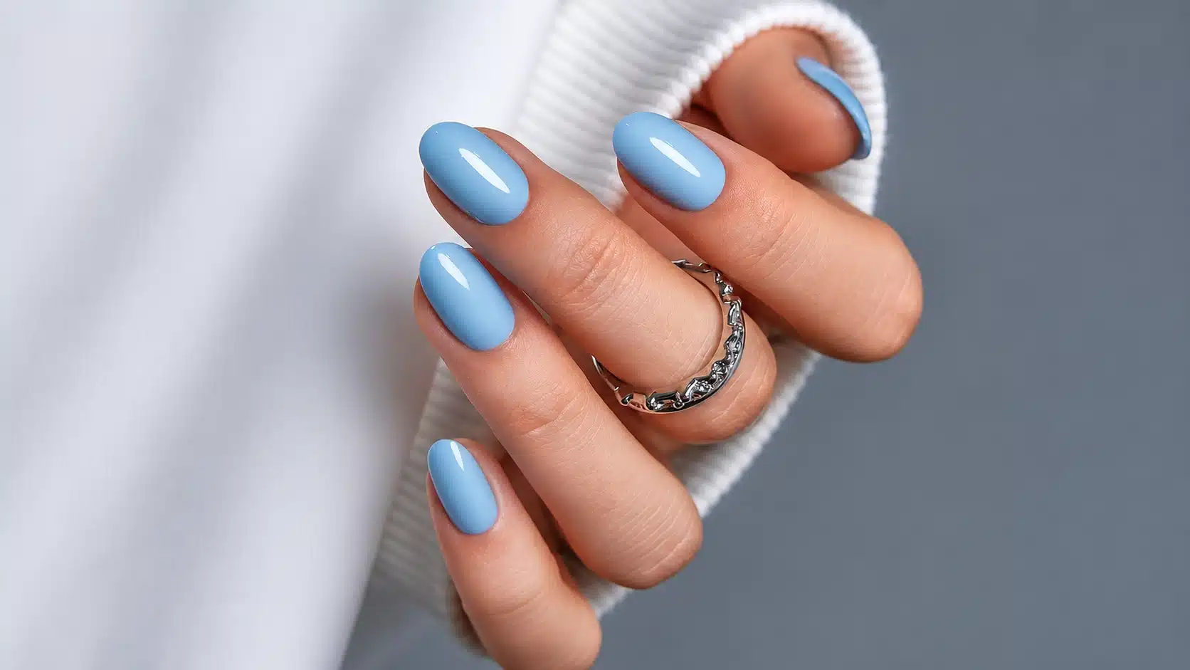 Glossy pastel blue oval nails with a silver crystal ring and white sweater sleeve