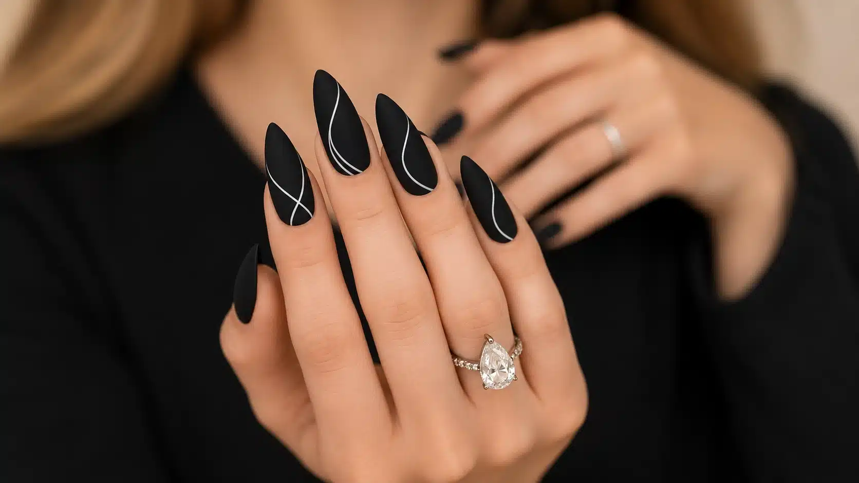 Long matte black stiletto nails with fine white swirl lines and a pear-shaped gemstone ring