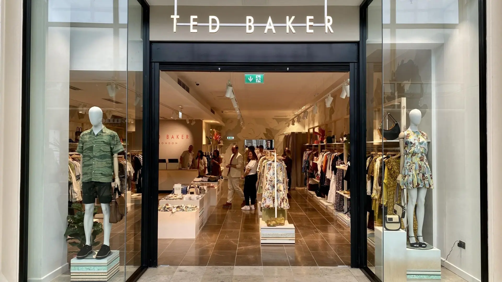 Ted Baker clothing store entrance with mannequins displaying casual outfits and racks of apparel visible inside.