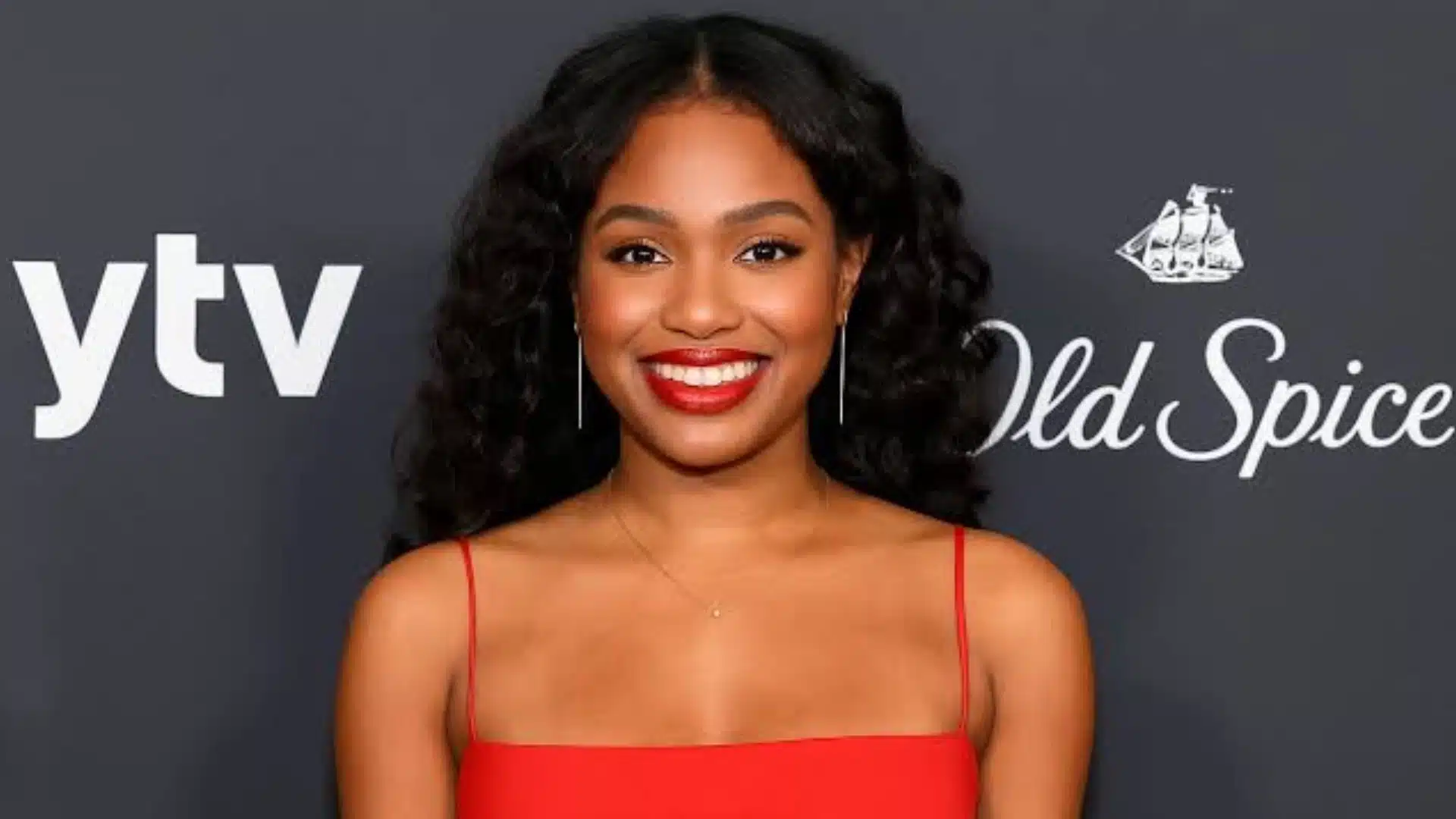 An individual in formal attire attending Old Spice Gala, with a vibrant atmosphere and guests in the background.