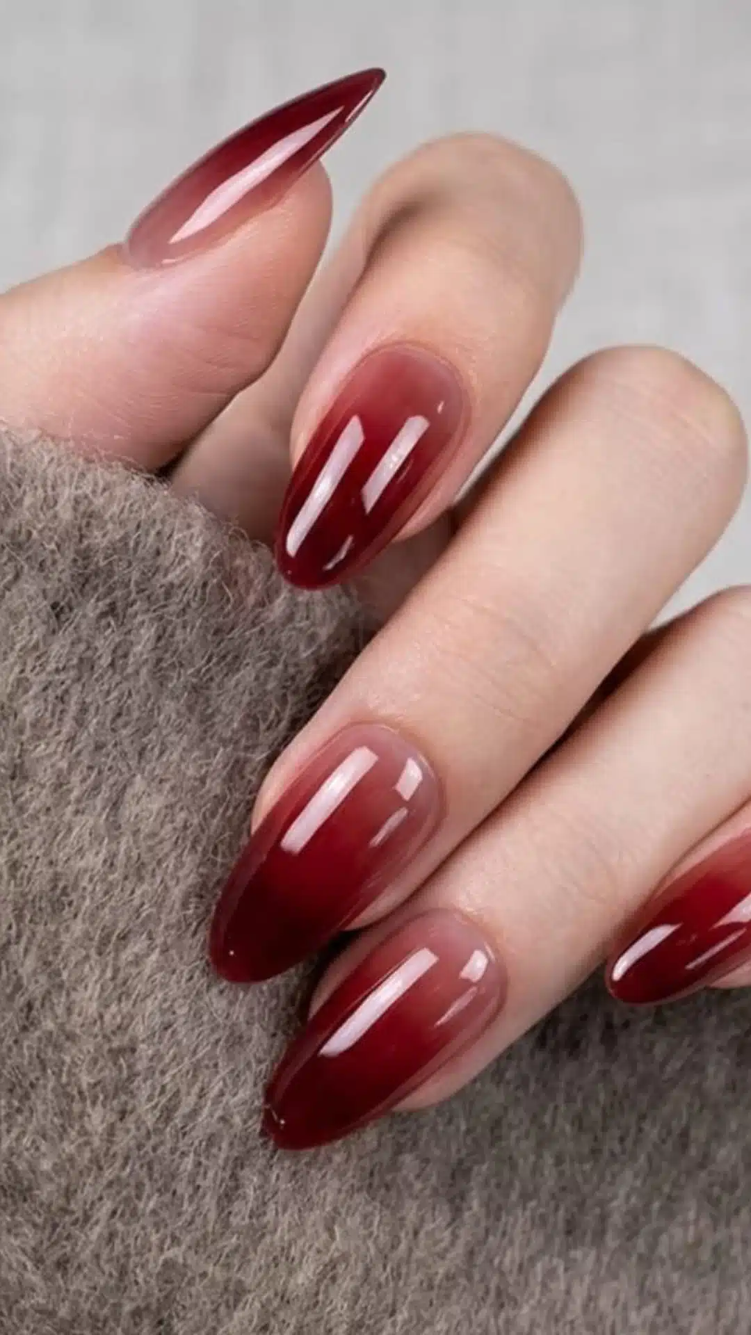 Wine red to nude ombre nails against a knit sweater