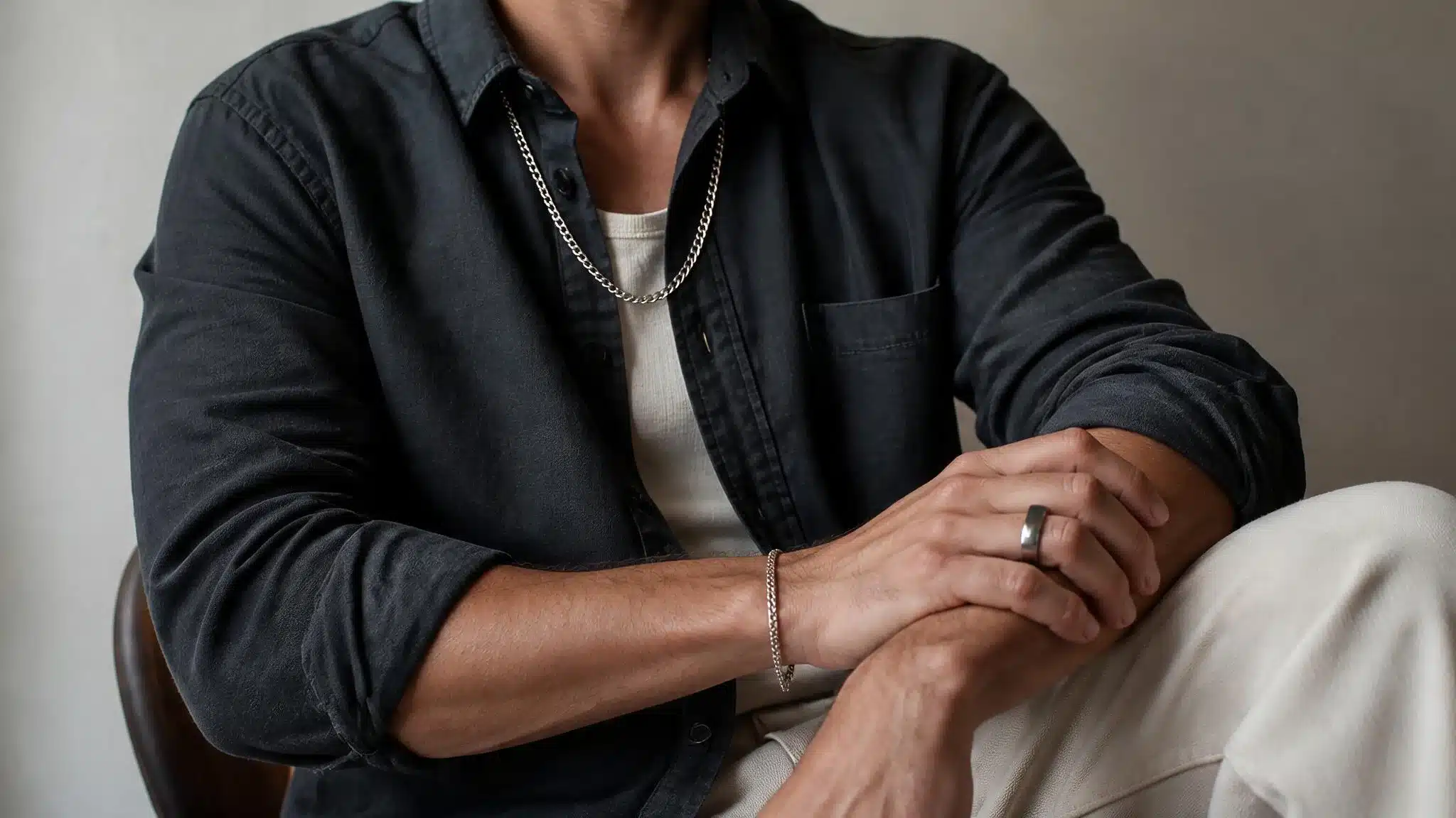 A man seated on a chair with his arms crossed, displaying a relaxed yet contemplative posture.