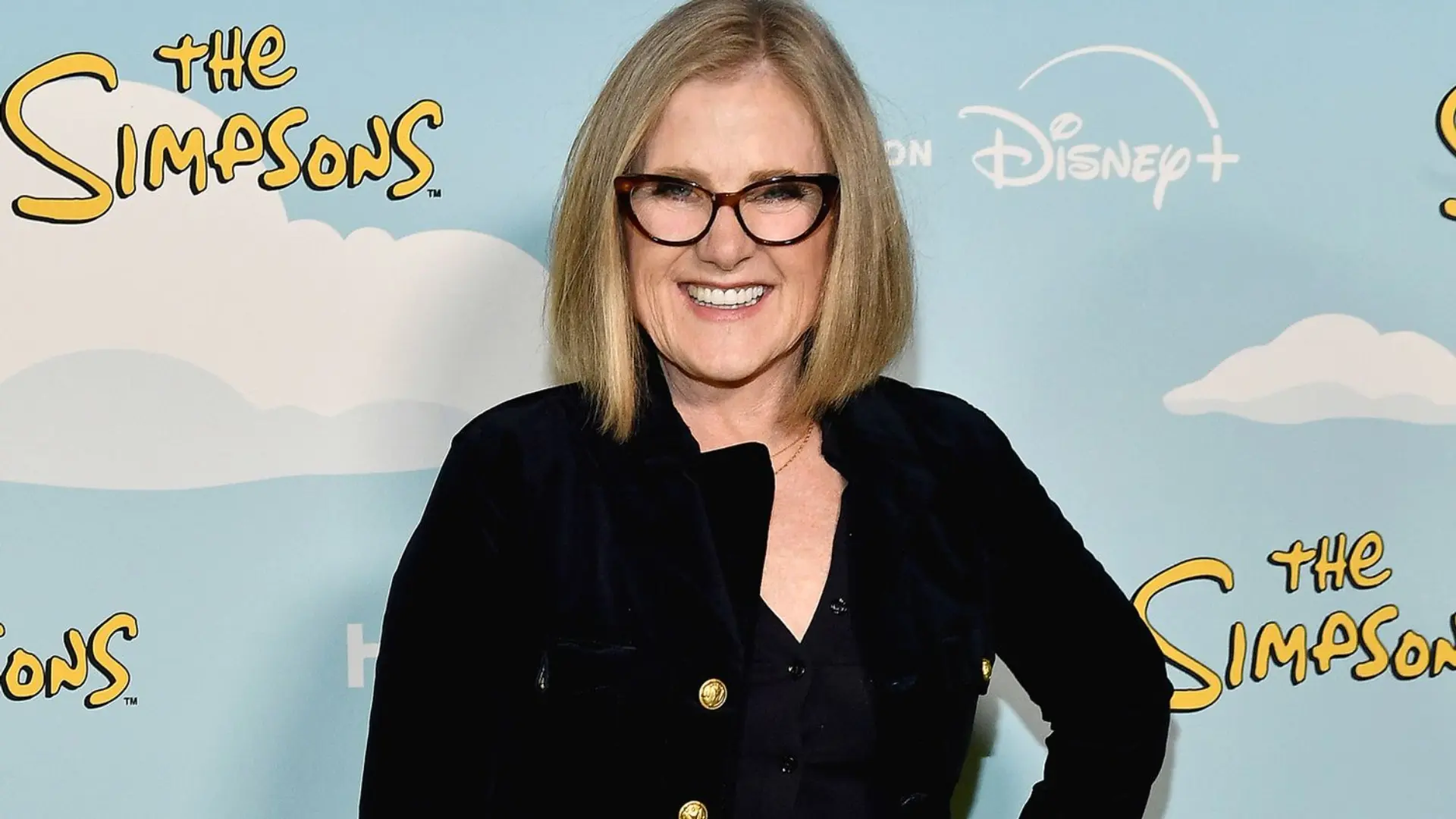 Nancy Cartwright smiling in glasses in front of a Simpsons backdrop