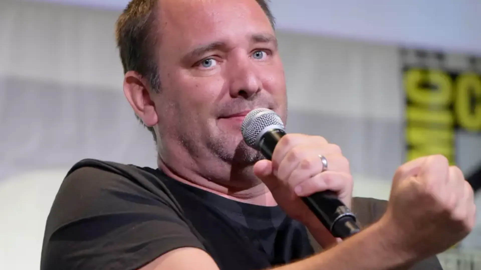 Trey Parker holding a microphone while gesturing with a raised fist at a panel